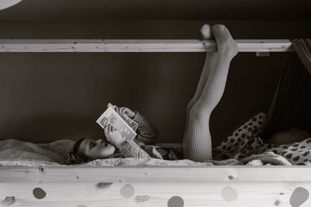 Meisje leest de Zoete Zusjes op bed, terwijl ze haar voeten in de lucht heeft. 