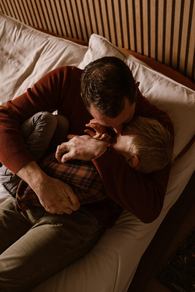 Vader en zoon liggen op bed en geven elkaar een dikke knuffel. 