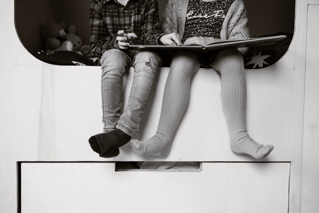 Zwart/wit foto van twee paar voeten van kinderen, terwijl ze met elkaar aan het lezen zijn. 