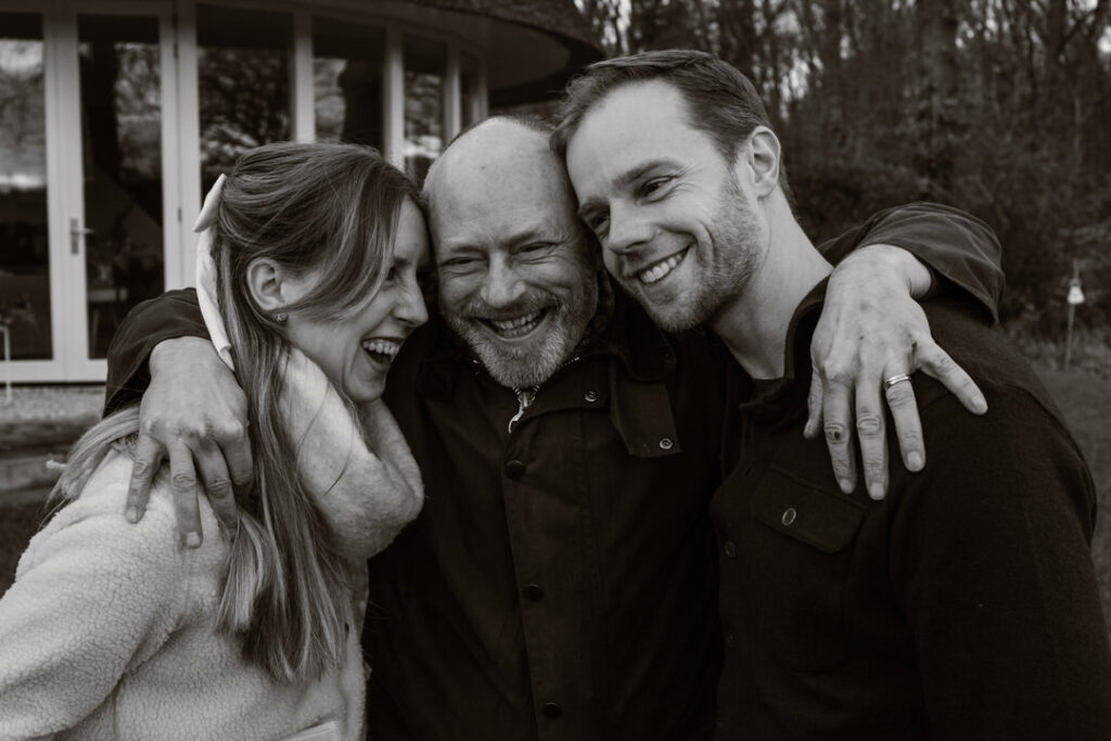 Man heeft zijn armen om zijn volwassen zoon en dochter geslagen terwijl ze alle drie aan het lachen zijn. 