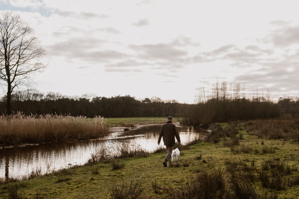 Man met witte hond wandelt langs de rivier de Regge bij Ommen